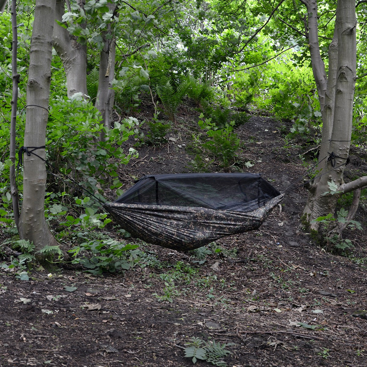 DD Frontline Hammock i Multicam hengt opp mellom to trær i en grønn løvskog, med myggnettet lukket