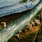 Olivengrønt DD Hammock Sleeve trukket over en hengekøye mellom to trær ved sjøen