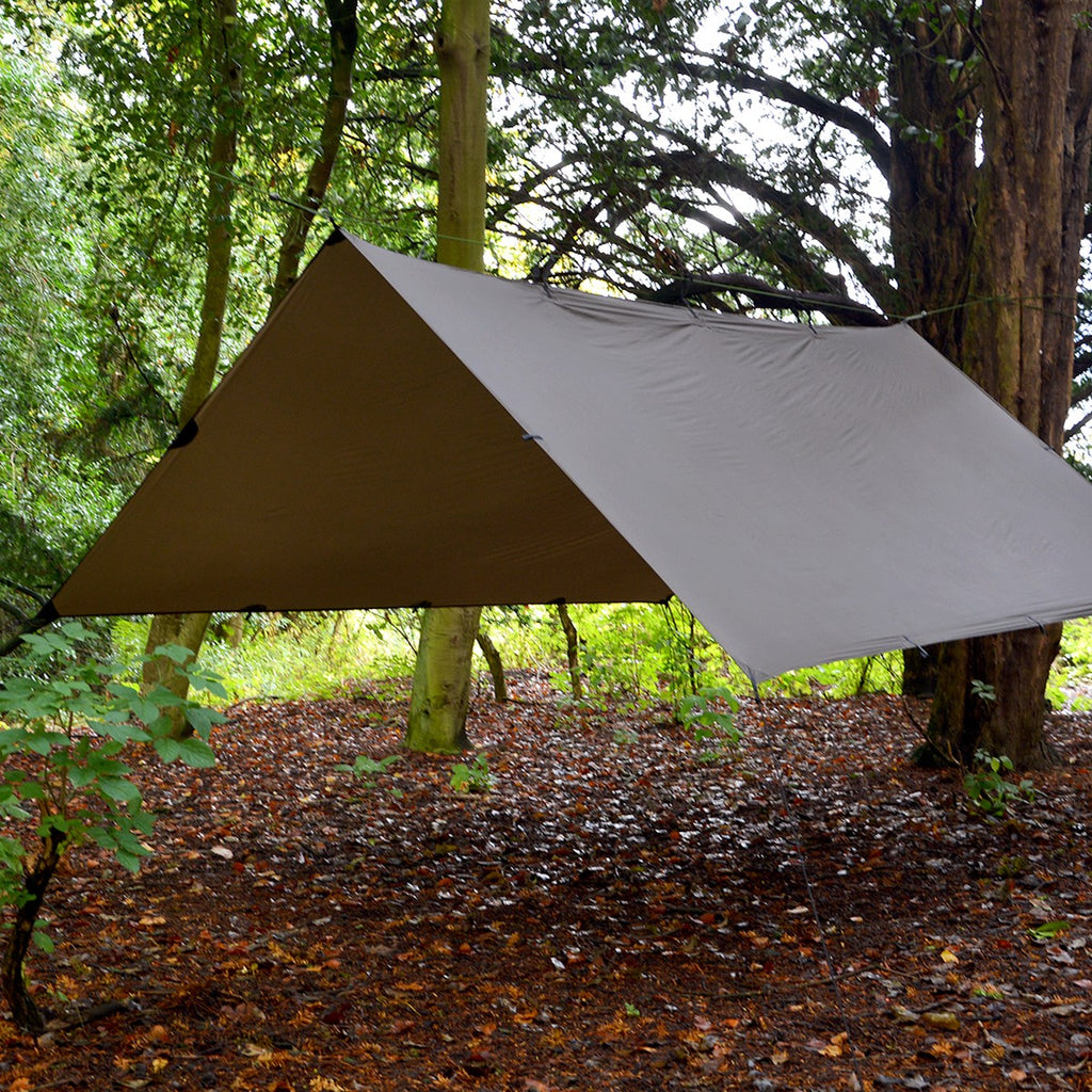 DD SuperLight Tarp i Coyote Brown satt opp som tak mellom trærne i en løvskog