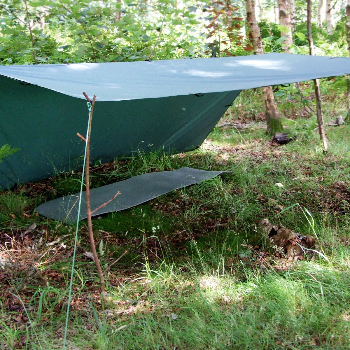 DD Tarp 3x3 i Olivengrønn satt opp som gapahuk med en kjepp foran og et liggeunderlag under